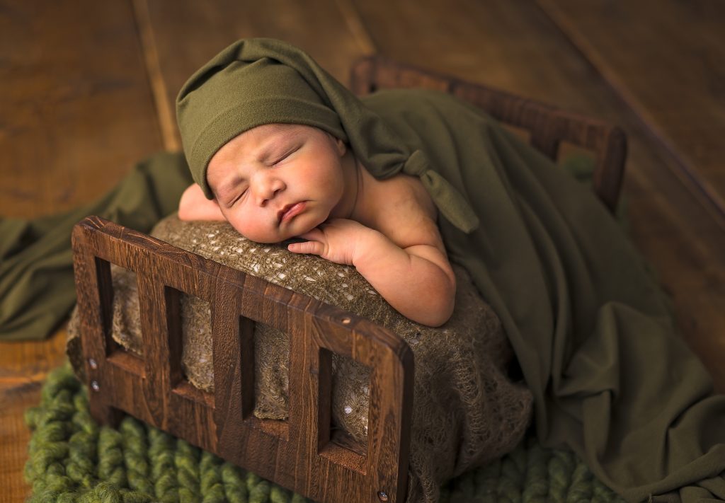 Newborn Baby Sleeping on a Bed with Green Sleeping Cap